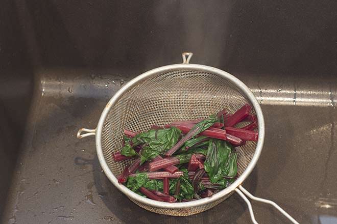 Cooked beet greens and stems draining in a wire mesh colander. 