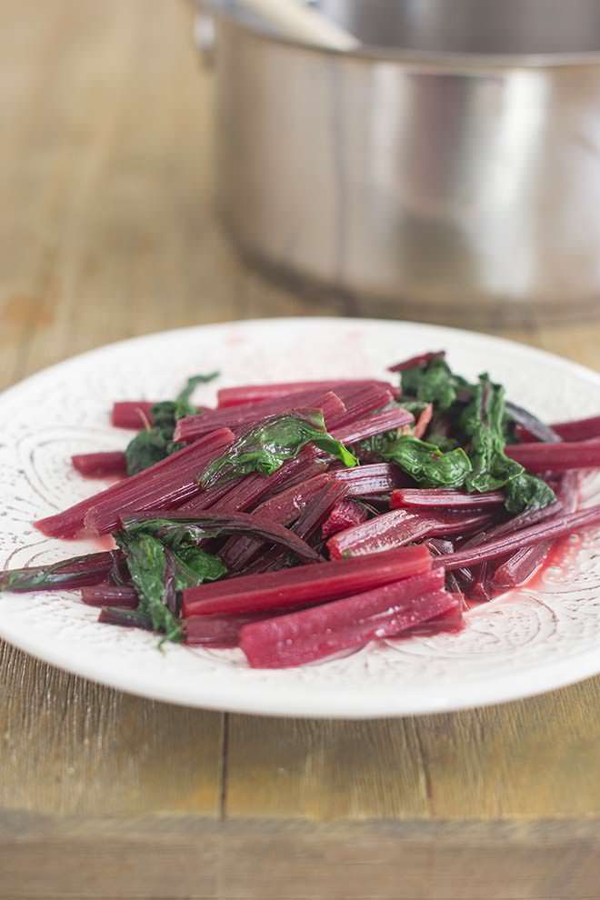 The stems and leaves from beets, cooked and on a white plate.
