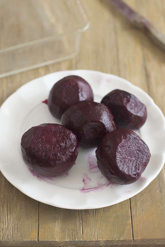 Roasted and peeled beets on a white plate.
