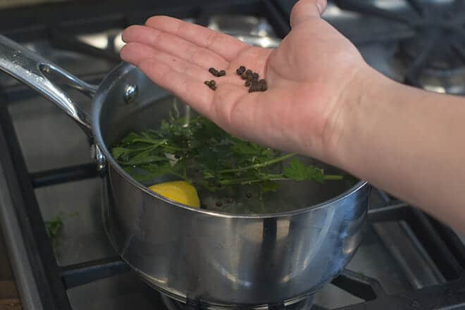 Peppercorns in hand over pan with water, lemon, and fresh parsley.