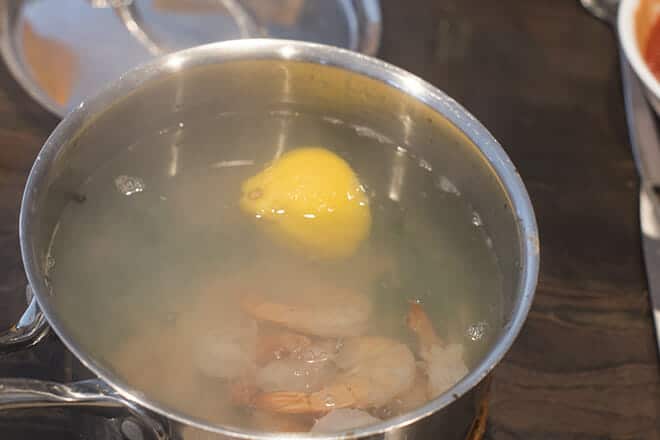 Frozen shrimp in the pot of hot water with a lemon half.