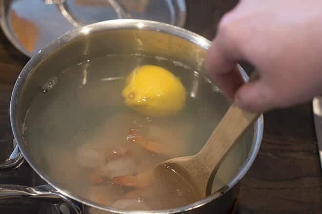 Shrimp and lemon half being stirred in hot water in saucepan.