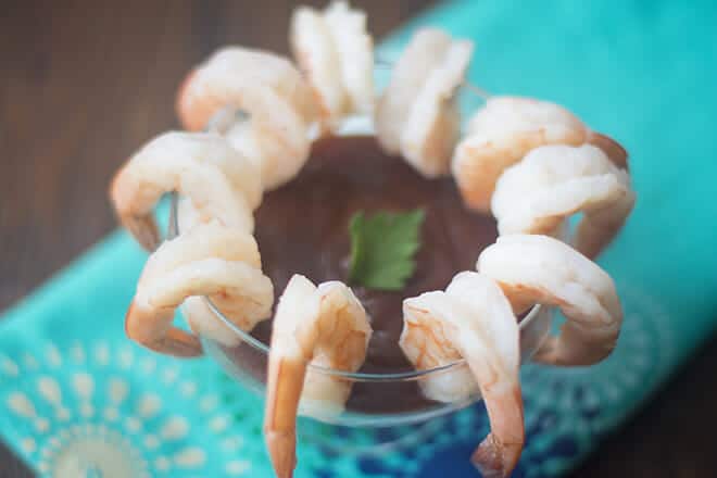 10 shrimp hanging around a glass with cocktail sauce inside.