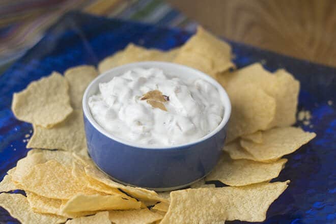 Homemade French Onion Dip in a small blue bowl, surrounded by potato chips.