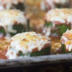 Zucchini slices topped with tomato sauce and mozzarella cheese on a baking sheet.