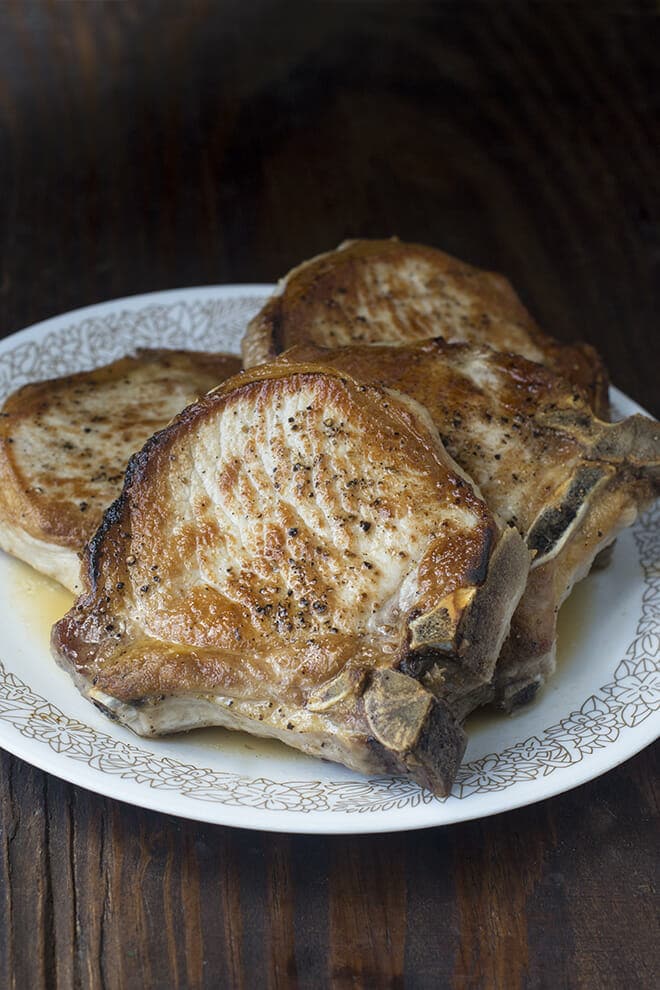 Four bone-on pork chops on a white dinner plate with a patterned rim.