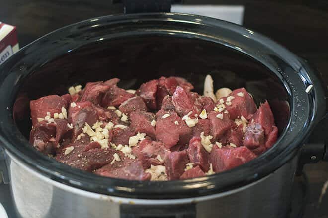 Stewing beef chunks with salt, pepper, and garlic in a slow cooker.