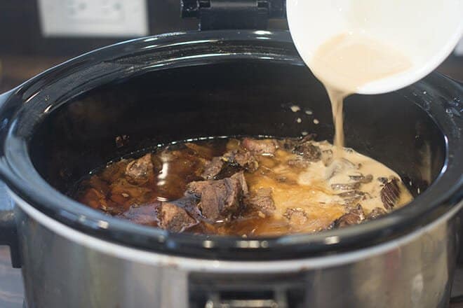 Pouring cornstarch mixture into the slow cooker with beef.