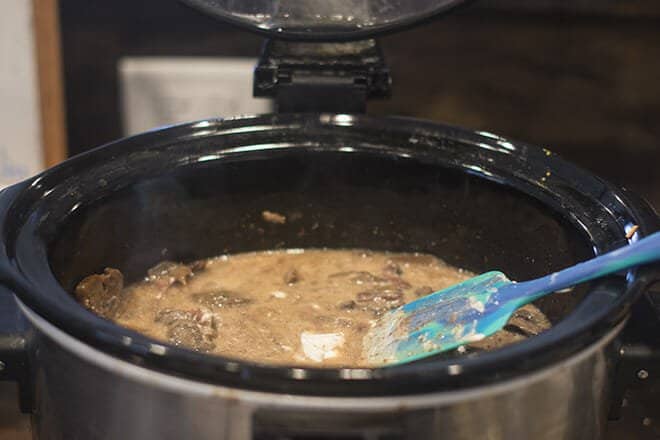 Sour cream being stirred into the beef stroganoff in the slow cooker.