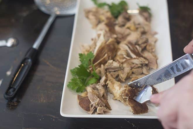Chicken shawarma being shredded with fork and knife.