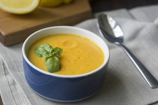 Blue bowl of butternut squash soup topped with fresh basil leaves.