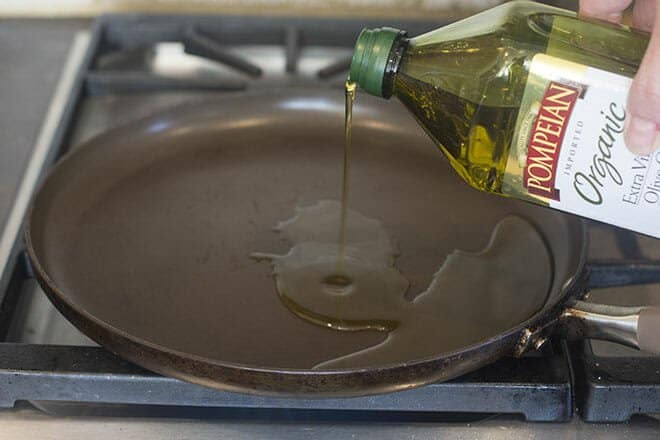 Olive oil being poured onto a pan on the stovetop.