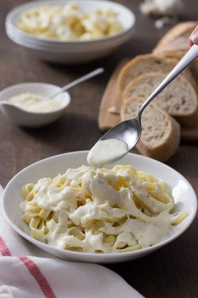 Thick and creamy alfredo sauce on fettuccine noodles in a white bowl.