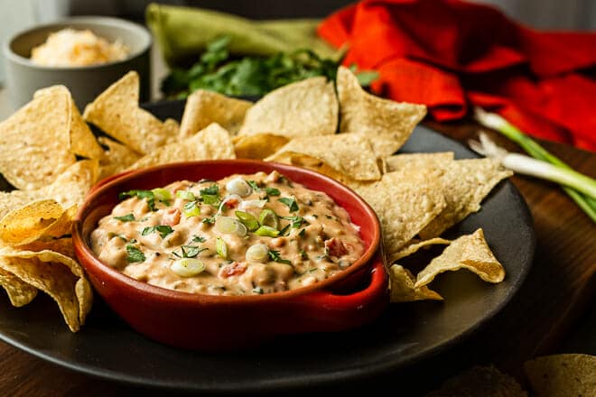 Nacho Dip topped with green onion in red bowl, surrounded by tortilla chips.