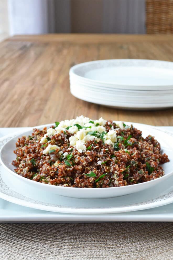 Red quinoa on a white dish topped with crumbled feta and parsley