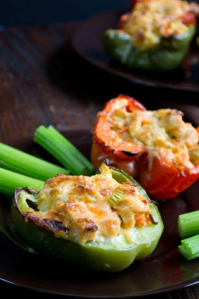 Halved bell peppers baked with chicken and cheese on a plate with celery sticks.