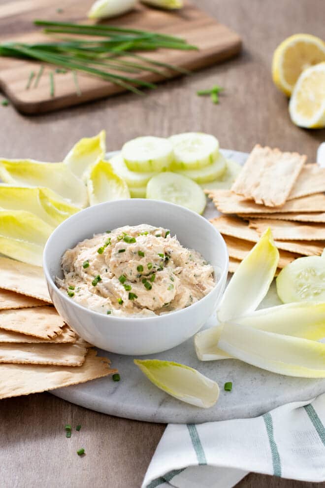 Smoked trout dip in a white bowl surrounded by crackers and veggies.