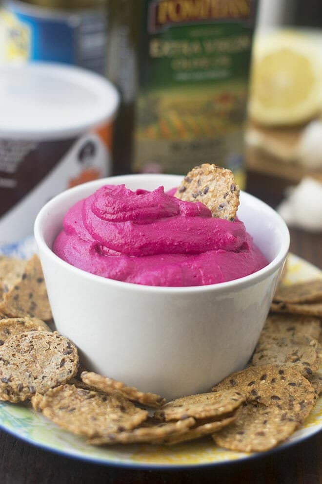 Roasted Beet Hummus in a white bowl surrounded by seeded crackers.