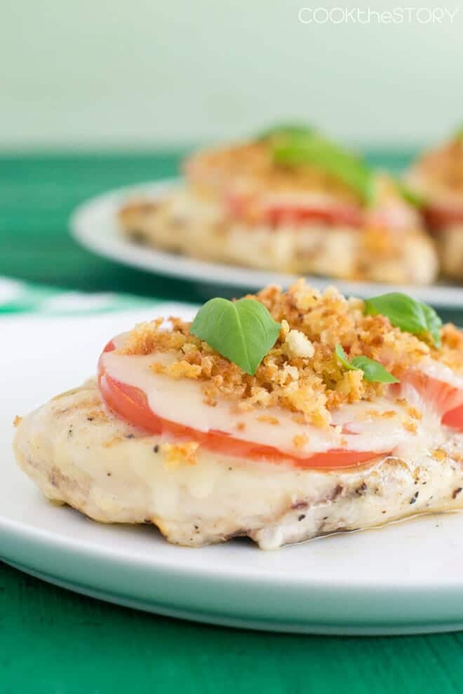 Chicken breasts topped with tomato slices, melted cheese, breadcrumbs, and fresh basil.