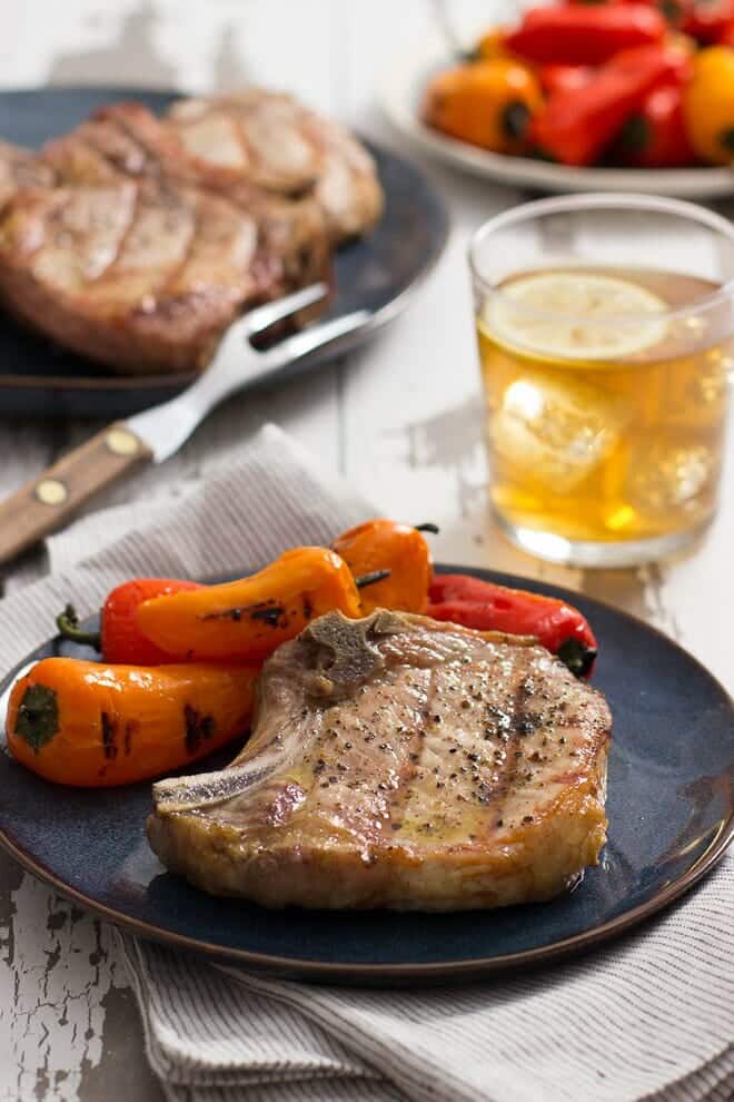 Grilled pork chop on a dark plate with grilled peppers.