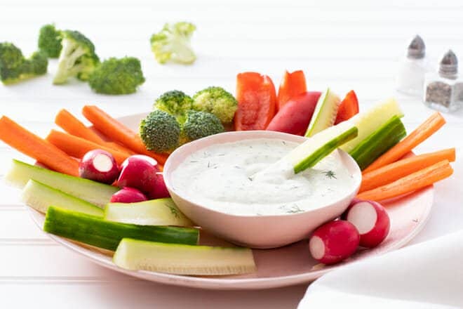 Bowl of Ranch Dip surrounded by fresh cut veggies like carrots, bell peppers, and broccoli.