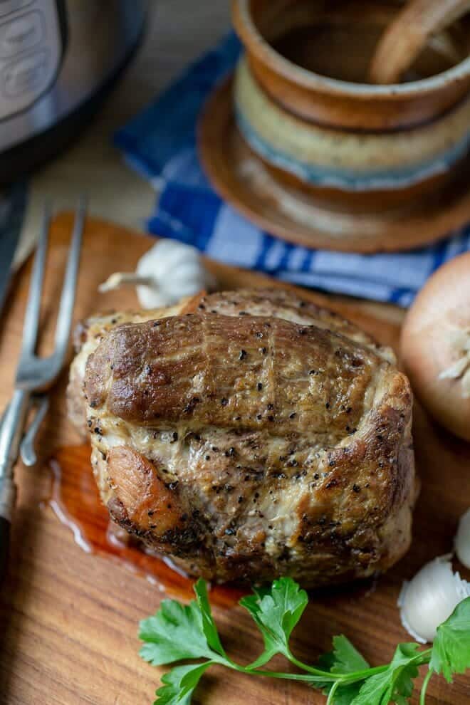 Pork roast on a cutting board with onion and garlic.