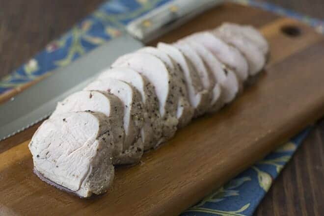 Sliced pork tenderloin on a wooden board.