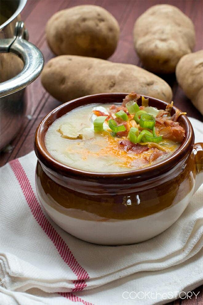 Bowl of loaded potato soup with potatoes in background.