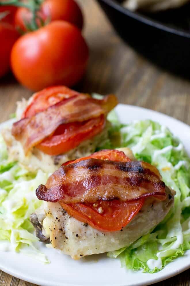 Chicken topped with tomato and bacon over lettuce on a white plate.