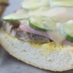 Open face sandwich showing pork, ham, pickles, and melted Swiss cheese.