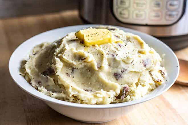 Bowl of mashed potatoes with skins and pat of butter on top.