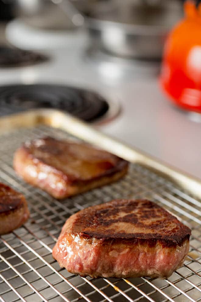 Seared steaks on a wire rack in a rimmed baking sheet.