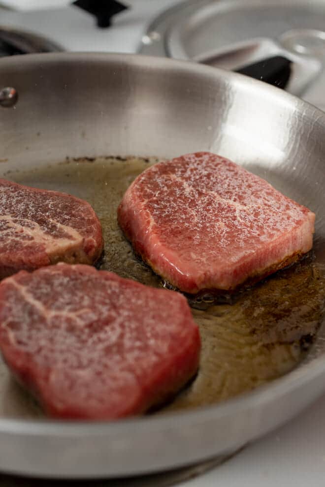 Three steaks in a skillet with oil.