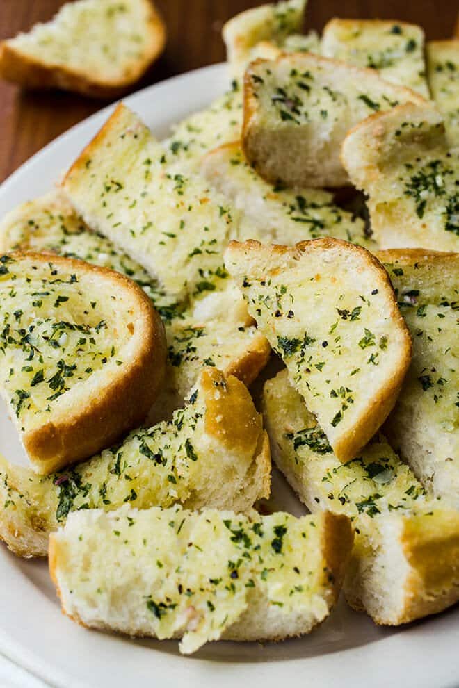 Delicious garlic bread cut in pieces on a white platter.