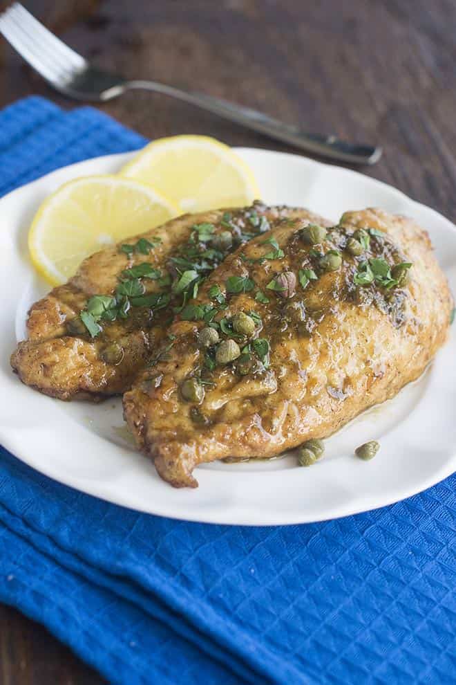 Chicken piccata on a white plate with lemon slices.