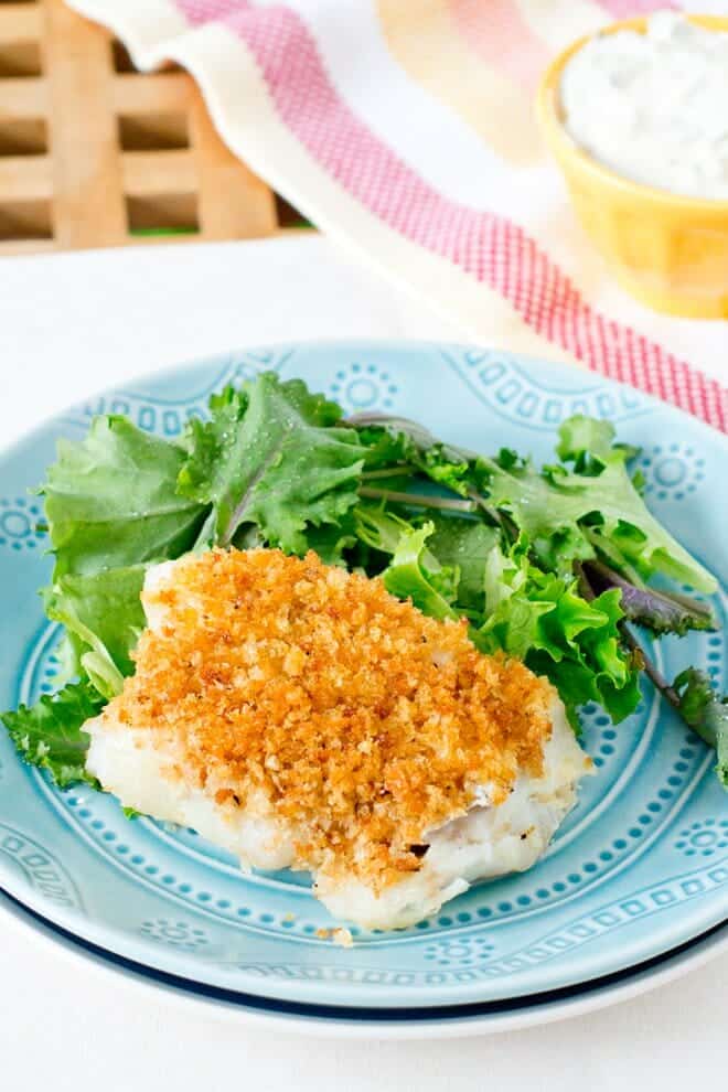 Fish fillet with breadcrumbs on a blue plate with salad greens.