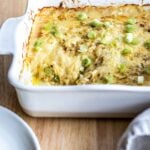 A white casserole dish with a cheesy potato casserole topped with green onions.