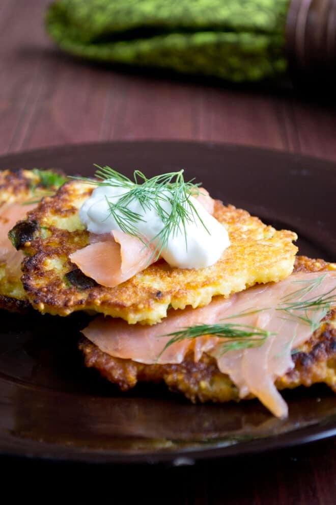 A stack of crispy browned millet pancakes topped with smoked salmon, sour cream, and dill