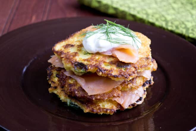 A stack of crispy millet pancakes topped with smoked salmon, sour cream, and dill.