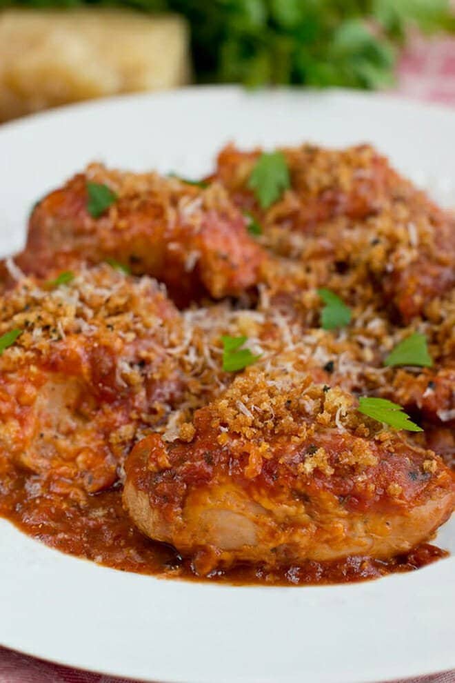 Chicken thighs on a white plate covered with tomato sauce, cheese, and breadcrumbs.