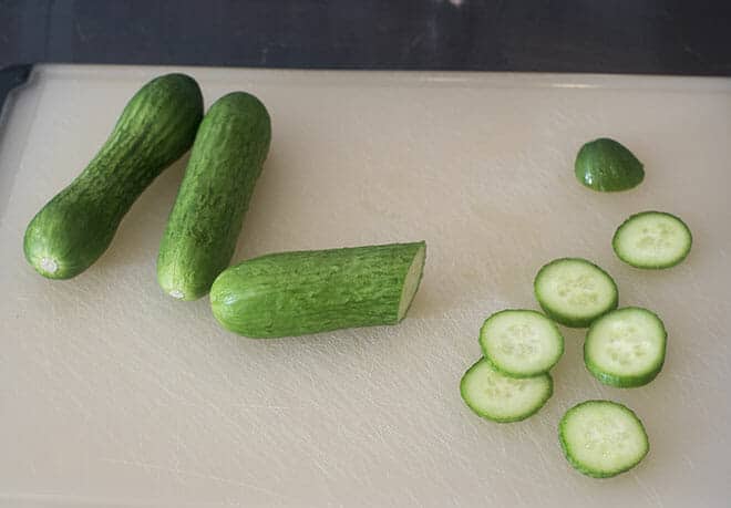 Three fresh cucumbers being sliced on a cutting board.
