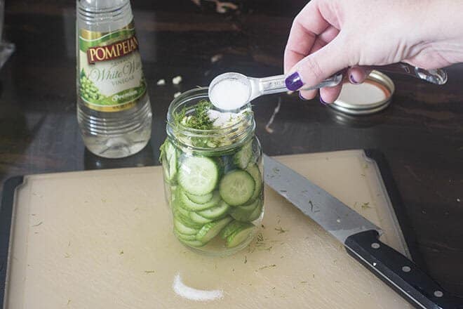Salt being added to glass jar of cucumber slices.