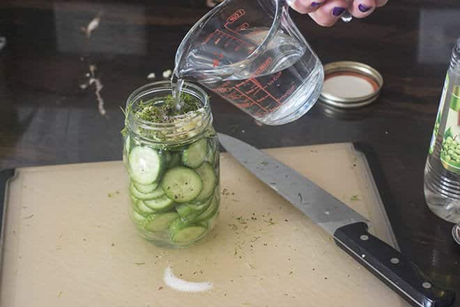 Liquid being poured into glass jar with quick pickle ingredients.