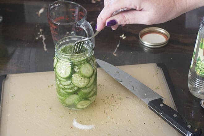 Cucumbers being pushed down with fork to submerge in liquid.
