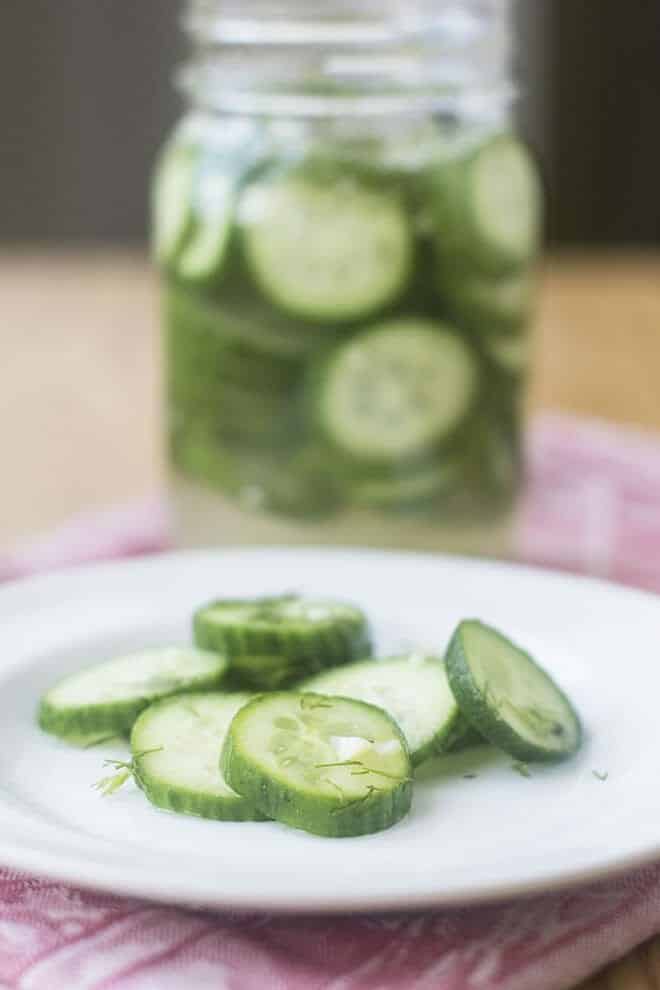Quick pickle slices on a white plate, jar of pickles in background.