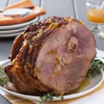 Bone in roast ham on a white serving plate with fresh thyme.