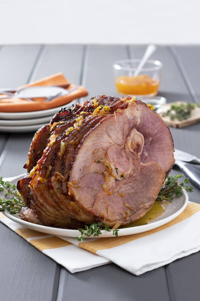 Bone in roast ham on a white serving plate with fresh thyme.