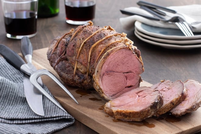 Roast lamb being sliced on a wooden cutting board.