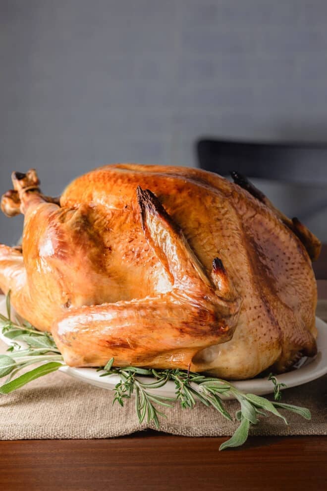 A turkey roasted until skin is crisp, with nicely browned skin, on a large platter surrounded by fresh sage leaves.