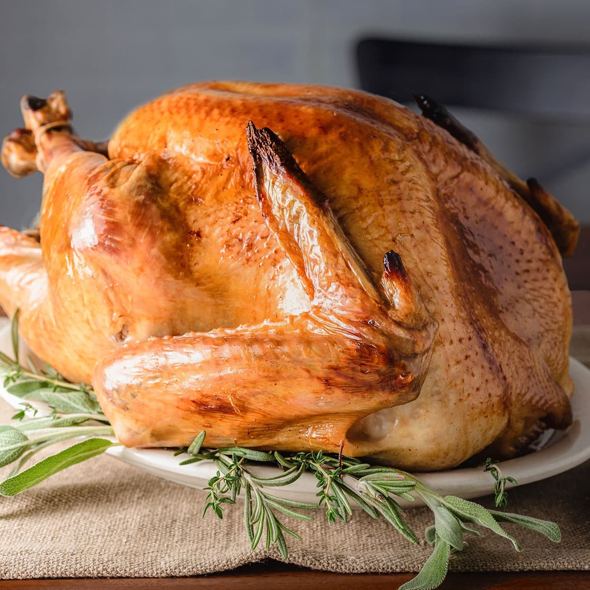 A roasted turkey that has crispy skin and a deep brown color, on a large platter surrounded by fresh sage leaves.